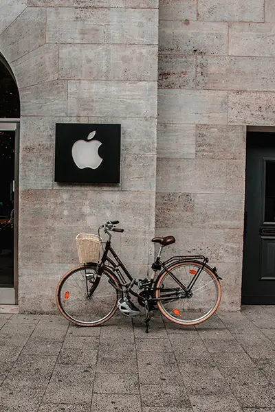 Apple Logo an einer modernen Steinwand mit einem Fahrrad davor, Symbol für minimalistisches Design und Innovation.