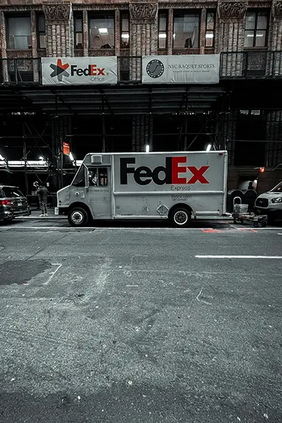 FedEx-Lieferwagen auf einer Straße, das Logo zeigt die globale Präsenz des Logistikunternehmens.